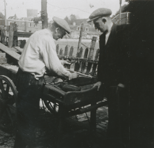 876890 Afbeelding van twee mannen bij een handkar met op de achtergrond een braakliggend terrein aan de nieuwe St. ...